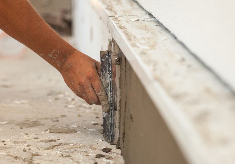 Man hand with trowel plastering a foundation of house